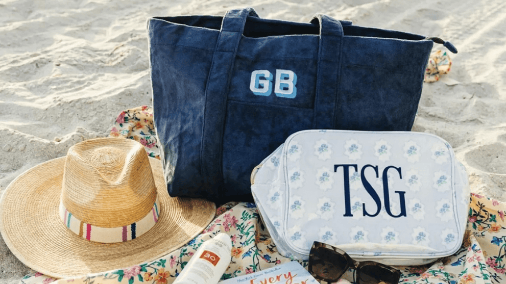 Toiletry Bag and Monogrammed Tote Resting On Beach