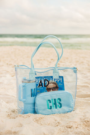 A blue clear tote with a navy and white monogram is set out at the beach.