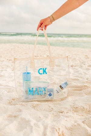 A person reaches for their white clear tote with a blue and mint monogram.