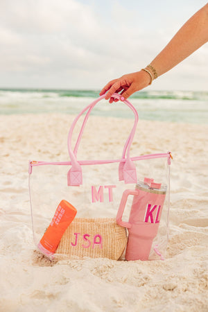A person reaches for their light pink clear tote with a pink monogram.