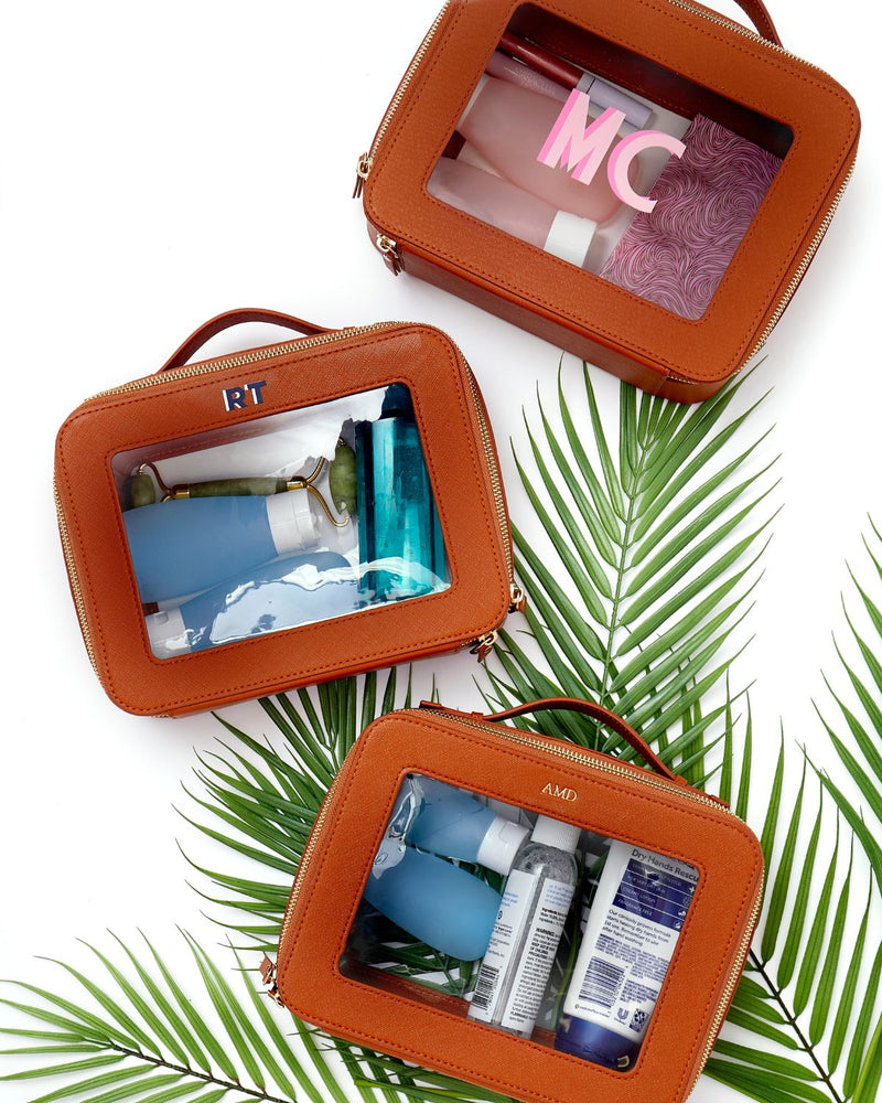 A group of tan clear leather toiletry pouches are monogrammed.