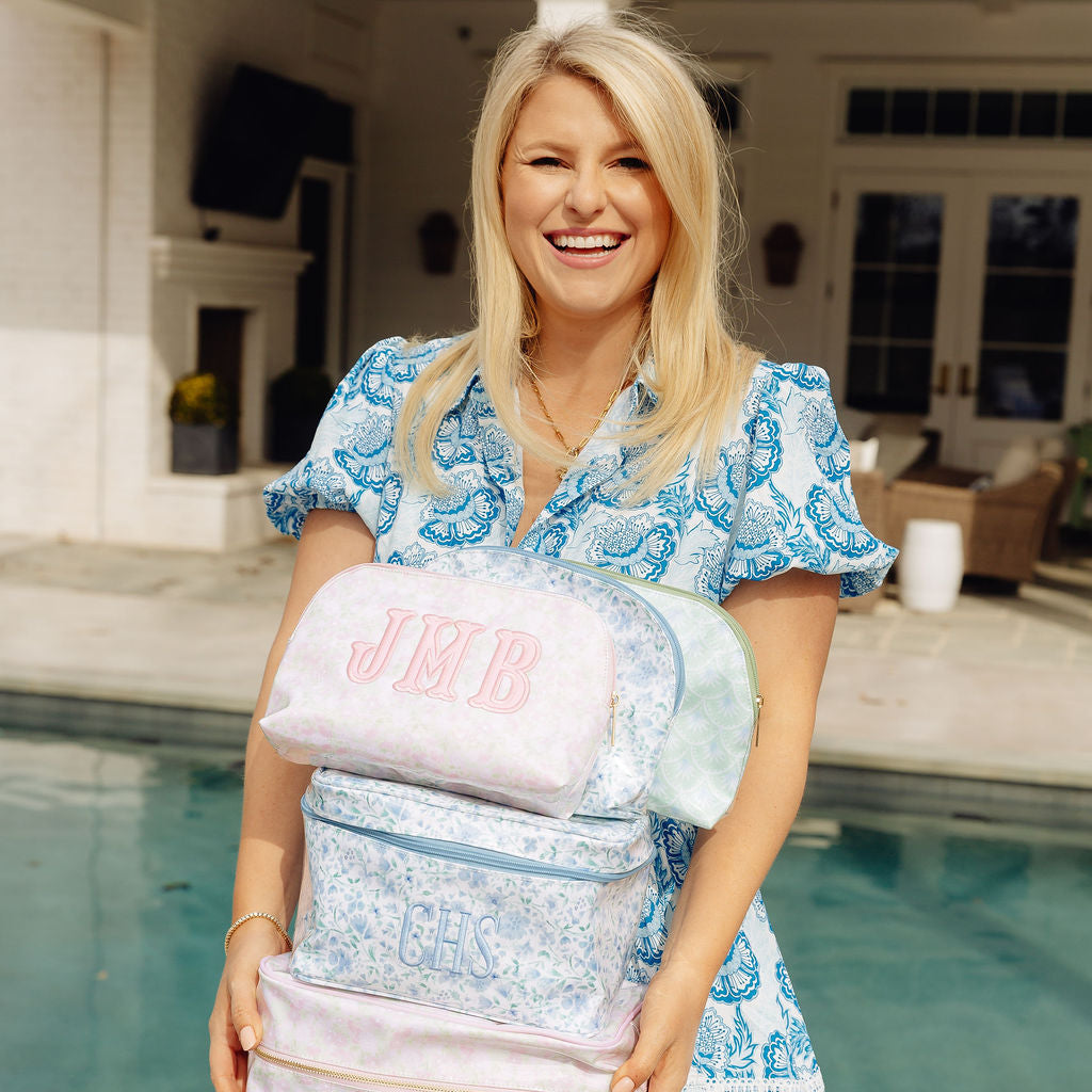 Woman holding a stack of clear bags with pink accents by a poolside.