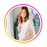 Woman wearing a white sweater draped over her shoulders, posing in a softly lit room with blue-and-white decor.