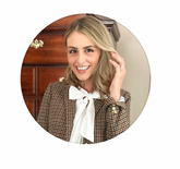 Woman smiling in a plaid blazer with a white bow blouse, posing indoors for a polished lifestyle portrait.