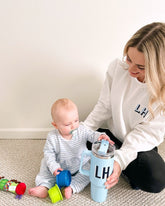 Woman wearing a white sweater with 'LH' initials, holding a blue tumbler with matching 'LH' initials