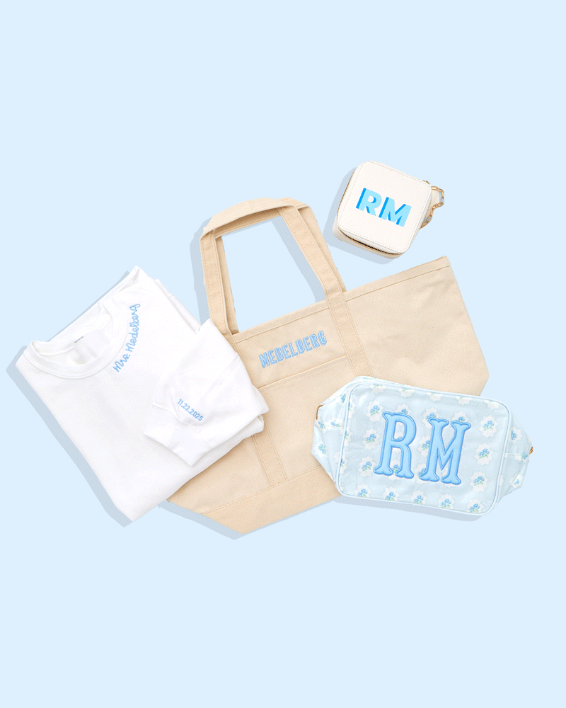 Custom bride gift bundle with embroidered 'Mrs.' white t-shirt, personalized canvas tote bag, monogrammed blue floral pouch, wallet, and keychain, styled on a pastel blue plaid background—perfect for bridal party gifting