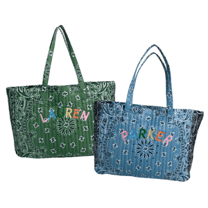 Two quilted tote bags with paisley bandana prints, one green and one blue, each personalized with a colorful embroidered name on the front.