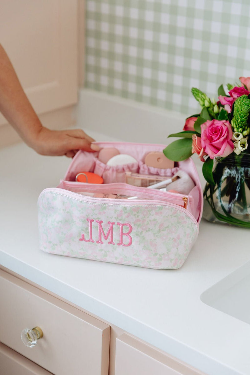 A pink floral clear-coated pouch monogrammed 'JMB' with organized interior compartments, styled with a rose bouquet
