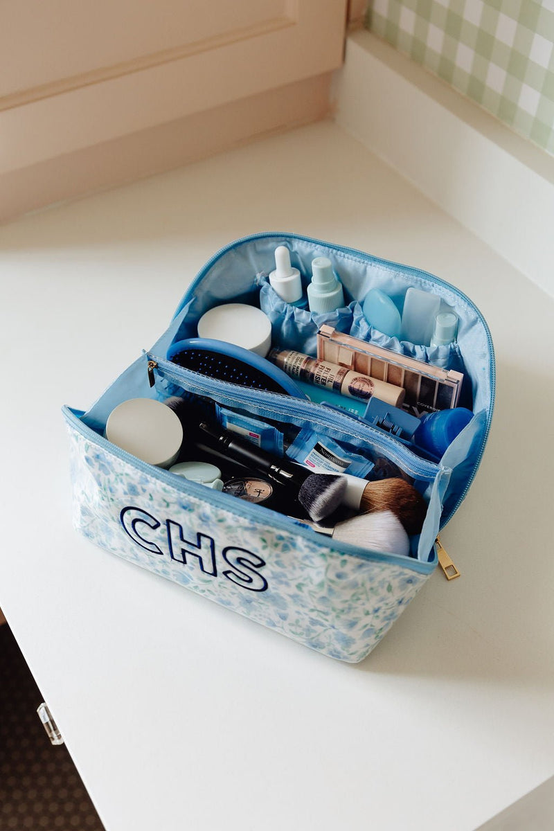 An open blue floral clear-coated pouch monogrammed 'CHS' packed with makeup and hair tools