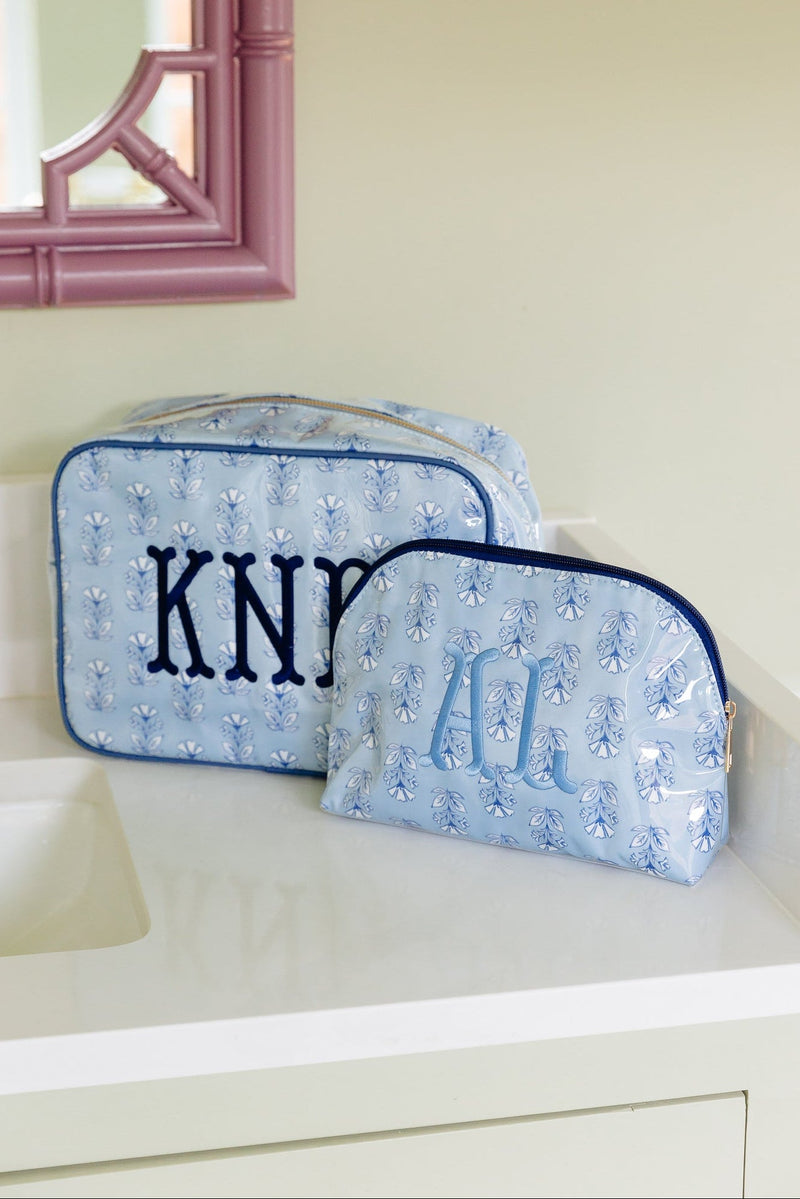 Light blue floral clear coated pouch monogrammed 'KNP' in navy and a smaller matching pouch monogrammed in light blue, on a bathroom counter.