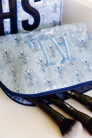 Close-up of an open light blue floral clear coated pouch monogrammed 'MW' in blue, beside a navy monogrammed pouch.