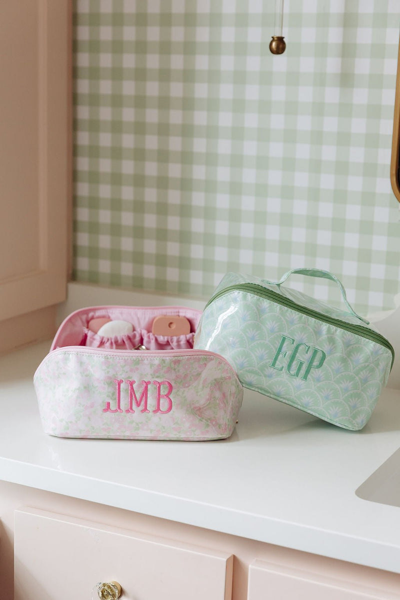 A pink floral pouch monogrammed 'JMB' and a green fan-print pouch monogrammed 'EGP' displayed together