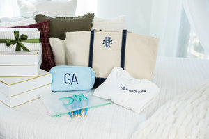 Teacher gift flat lay with a canvas tote bag, light blue monogrammed pouch reading 'GA', mesh pencil pouch, folded white sweatshirt embroidered 'Mrs. Williams', and wrapped gift boxes