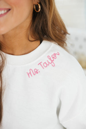 Close-up of 'Ms. Taylor' embroidered in pink script on the collar of a white sweatshirt