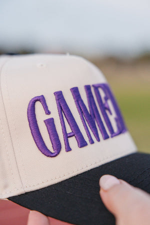 Close-up of raised purple “GAMEDAY” stitching on cream/black cap.