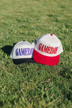 Navy- and red-brim caps on grass, each with raised “GAMEDAY”.