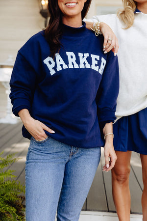 Two smiling women, one wearing a navy mockneck sweatshirt printed 'PARKER'