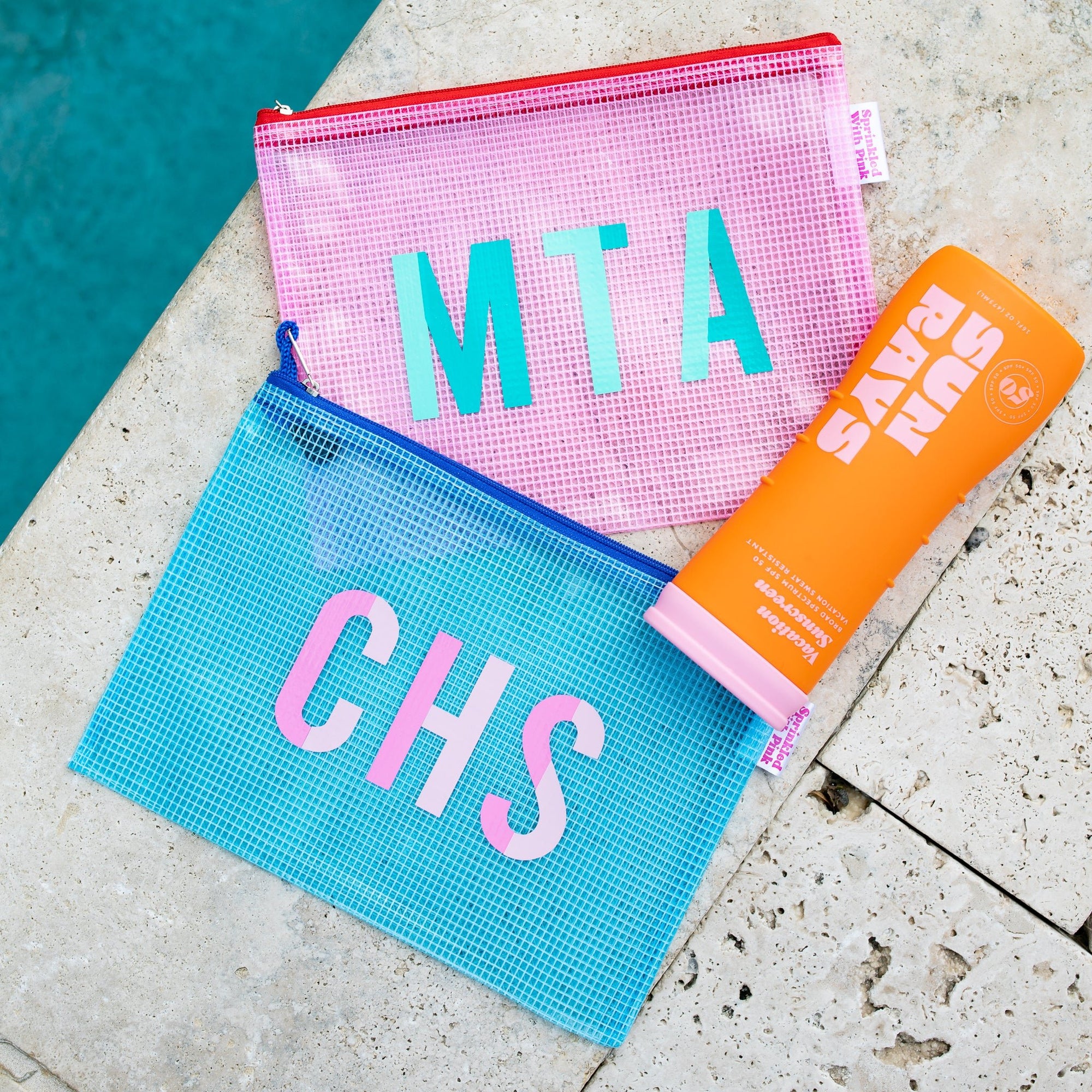 A pink, white, and blue pool bag are monogrammed with duo colored monograms.
