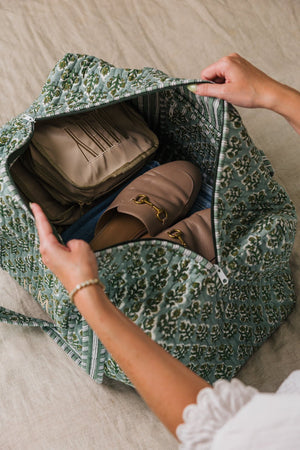 Open embroidered block print duffel showing spacious interior with shoes and travel accessories.