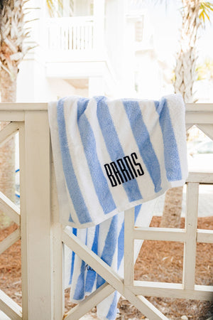 A blue cabana towel hangs over a railing and is customized with an embroidered last name.