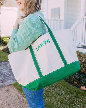 Woman smiling outdoors while carrying a large Embroidered Canvas Tote with green straps and base, personalized with the name “TARYN” in green thread—perfect for everyday errands or weekend getaways.
