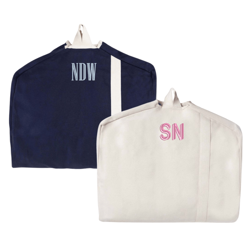 A stylish set of two personalized garment bags in navy and beige, each featuring custom monogram embroidery. The navy bag showcases "NDW" in light blue thread, while the beige bag is adorned with "SN" in soft pink. Designed for travel and organization, these canvas garment bags offer a chic and functional way to protect clothing while on the go.