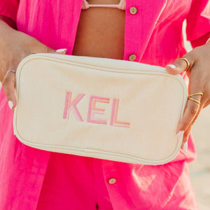 Neutral embroidered canvas pouch with pink monogram, stylish storage for daily essentials.