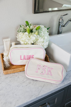 White embroidered canvas pouch with pink applique monogram, versatile accessory bag.