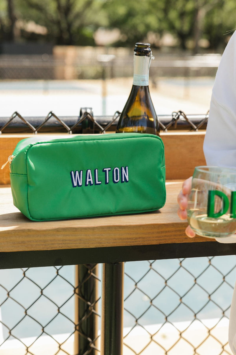 A green nylon pouch is embroidered with a navy and white name