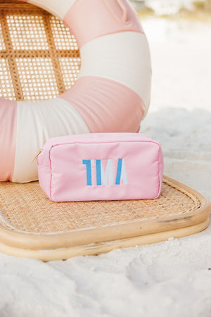 A pink nylon pouch is embroidered with a blue monogram at the beach.
