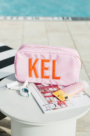 Pink nylon pouch with applique initials KEL styled in bright setting.