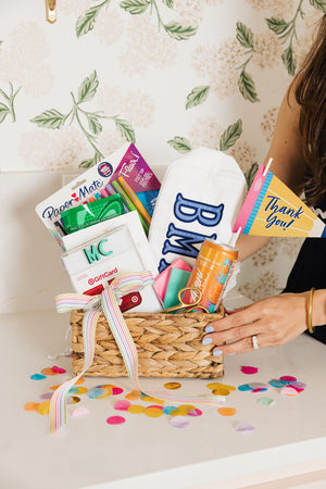 Gift basket with monogrammed pouch, pens, gift card, sparkling drink, and thank you flag with confetti.