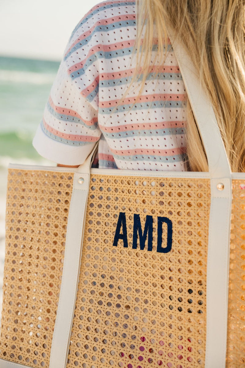 A girl in a striped shirt holds a canning tote with a navy embroidered monogram.