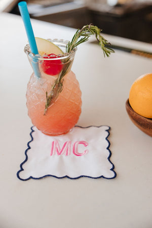 A fruity cocktail is placed on a navy scalloped cocktail napkin with a pink monogram.