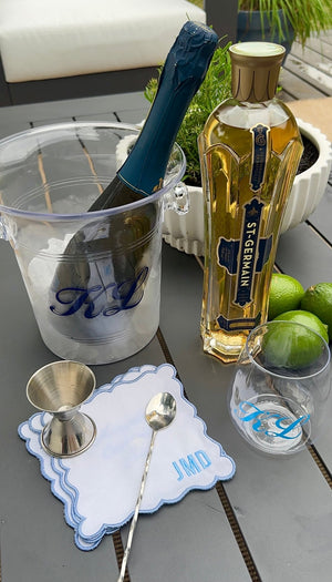Embroidered Monogram Scalloped Cocktail Napkins (Set of 4): white linen with baby-blue scalloped edge and “JMD” embroidery, styled with silver jigger and bar spoon