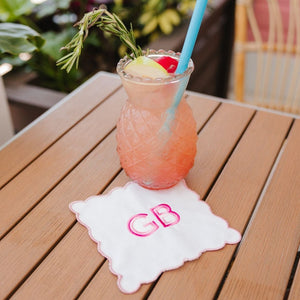 A fruity cocktail is placed on a pink scalloped cocktail napkin with a pink monogram.