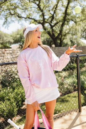 A girl throws a tennis ball into the air while wearing her customized tennis sweatshirt and monogrammed visor