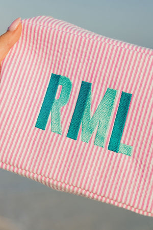 A pink seersucker pouch is embroidered with a mint and turquoise monogram.