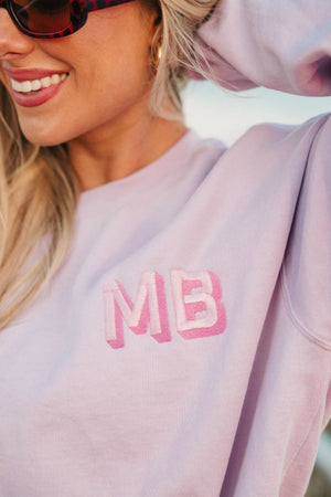 A woman poses in her purple sweatshirt with a pink embroidered monogram.