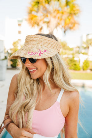 A woman by the pool wears a straw visor with a pink name embroidered on it.