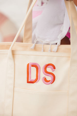 A cream coated canvas tote is customized with a pink and orange monogram.