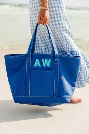 A blue coated canvas tote is customized with a mint and turquoise embroidered monogram