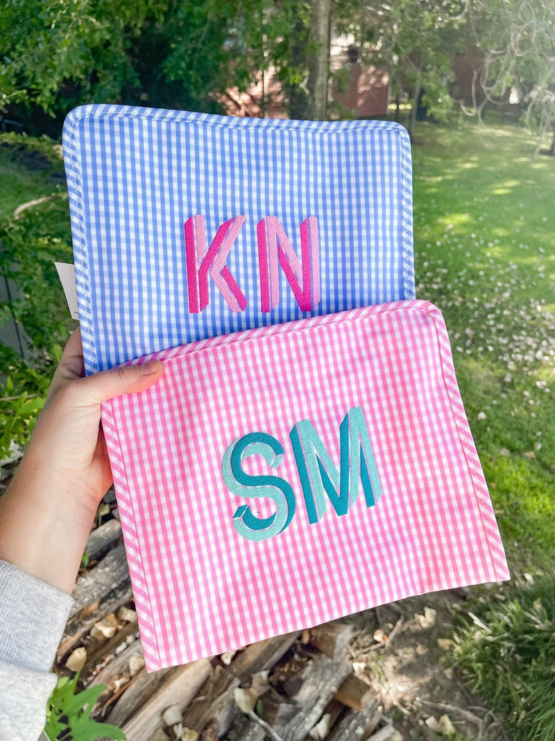 A person holds up a blue and pink gingham pouch with monograms embroidered on them.
