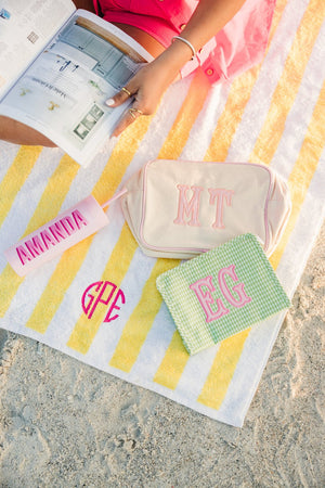 Colorful embroidered TRVL Roadie cosmetic bag with applique monogram on striped background.
