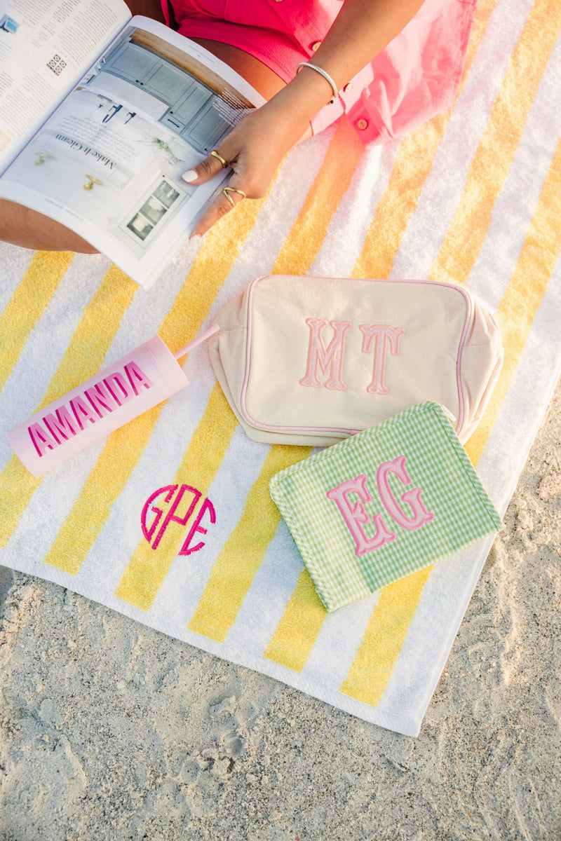 Colorful embroidered TRVL Roadie cosmetic bag with applique monogram on striped background.