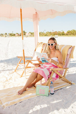Woman relaxing at the beach with embroidered TRVL Roadie applique travel pouch.