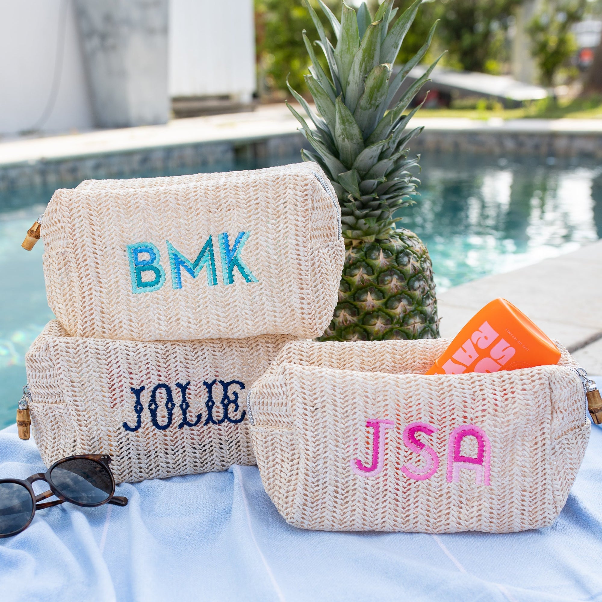 A straw pouch is customized with a name embroidered in navy font