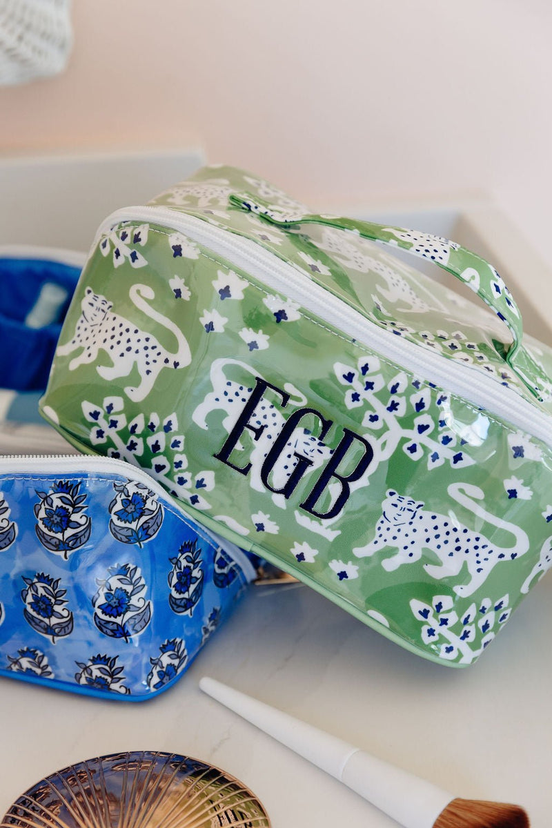 Close-up of a green leopard-print flat lay pouch monogrammed 'EGB' next to a blue floral pouch