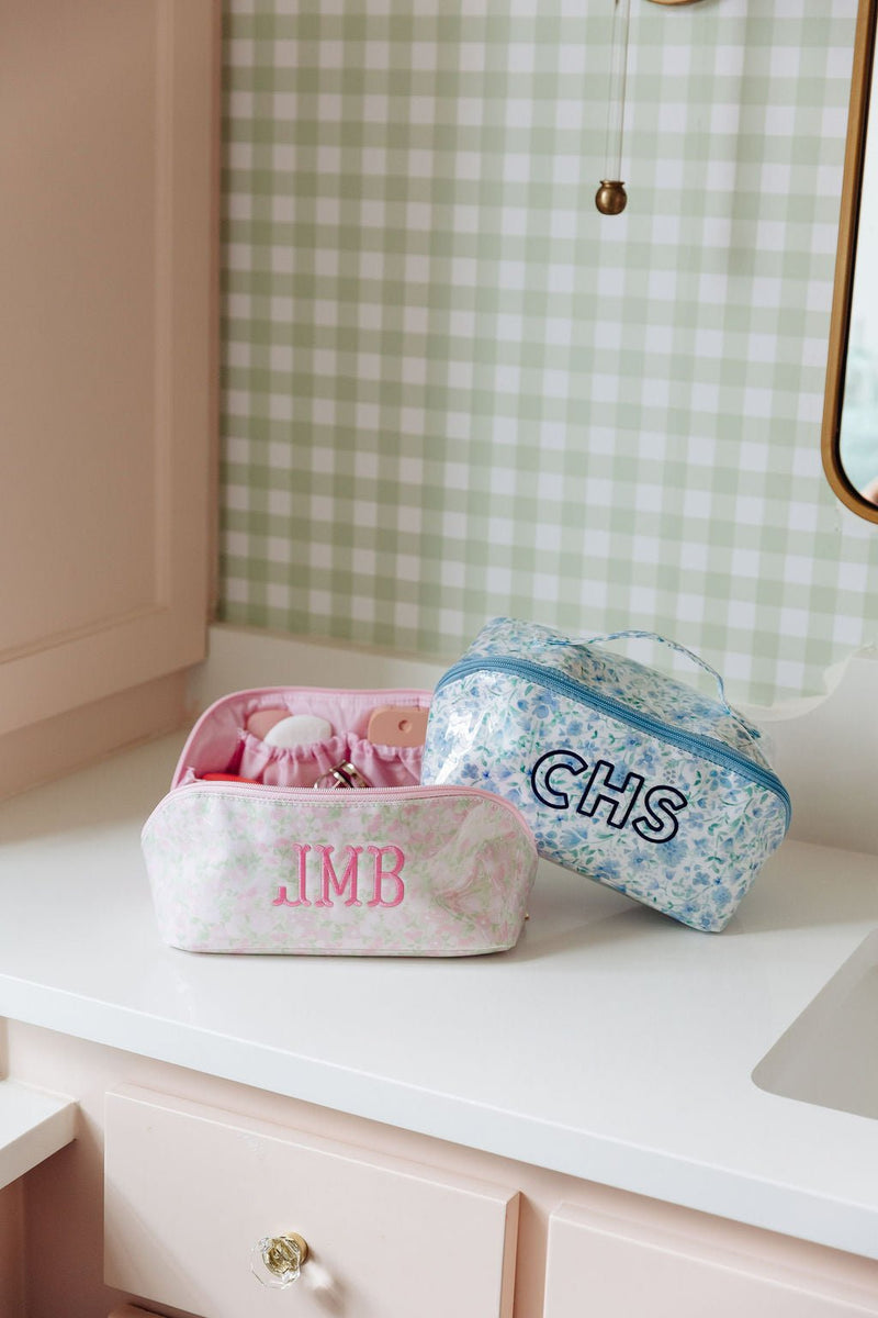 A pink floral pouch monogrammed 'JMB' and a blue floral pouch monogrammed 'CHS' on a bathroom counter