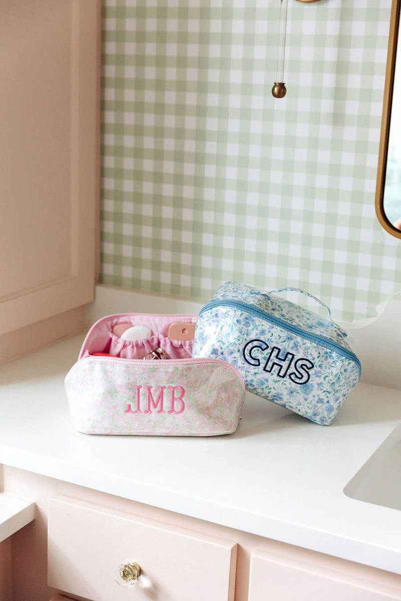 A pink floral pouch monogrammed 'JMB' and a blue floral pouch monogrammed 'CHS' on a bathroom counter